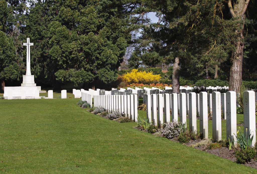 Row of white headstones with green grass in front.